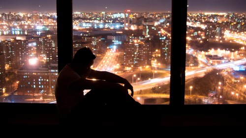 Depressed man sitting by the window, while the world passes by