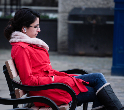 A woman sitting on a bend, with headphones